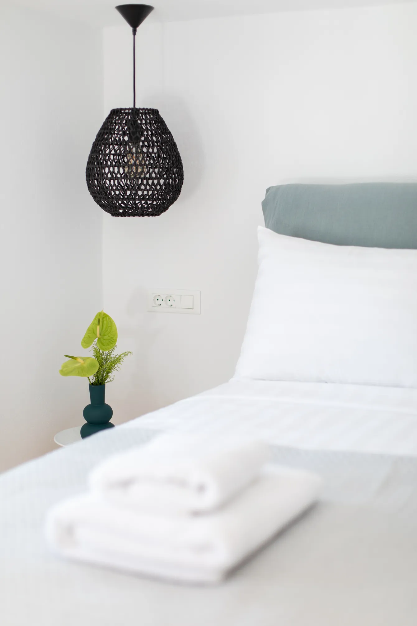 Bed with sage cushions and black pendant lamp